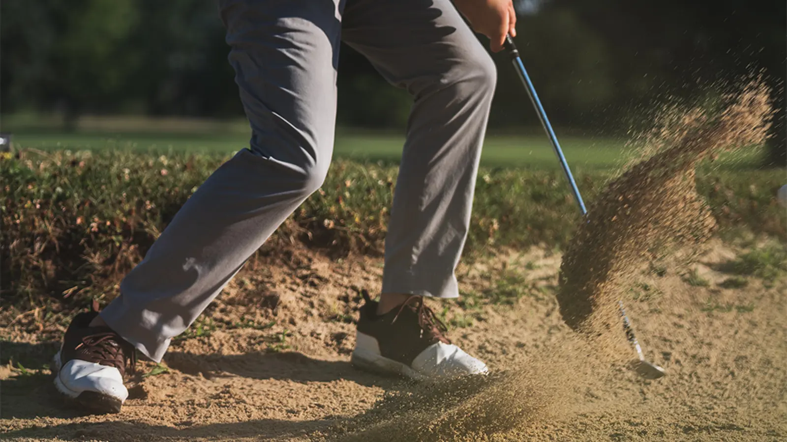 A man swinging a golf club in a sand bunker