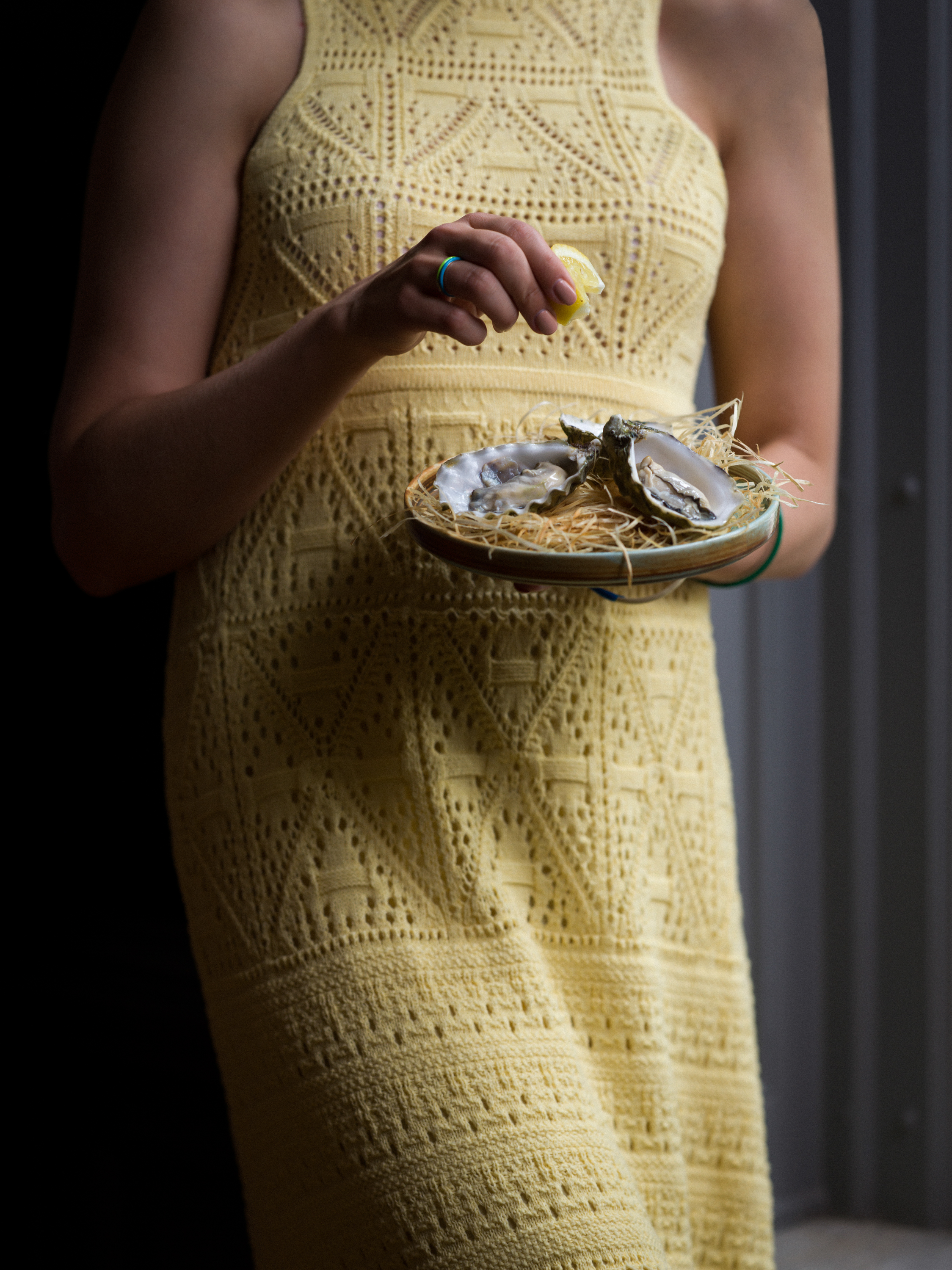 Woman in yellow dress holds a plate of oysters and squeezes a lemon over it