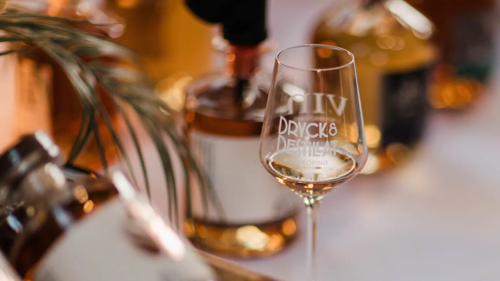 Glas med texten "Dryck & Destillat" med bakgrund av flaskor, event i Norrköping