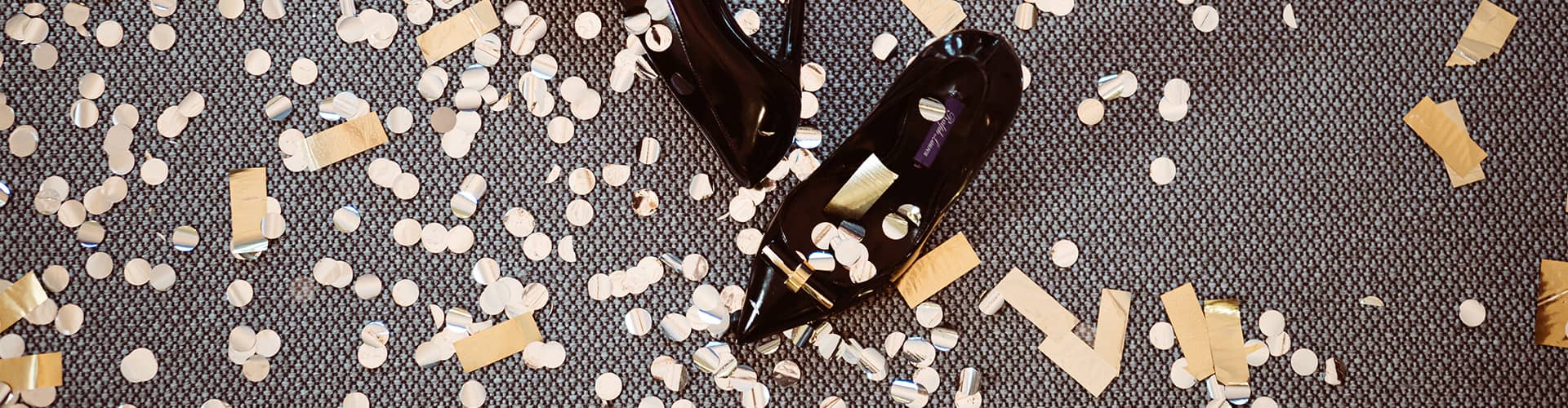Svarta högklackade skor på golv med guldigt confetti
