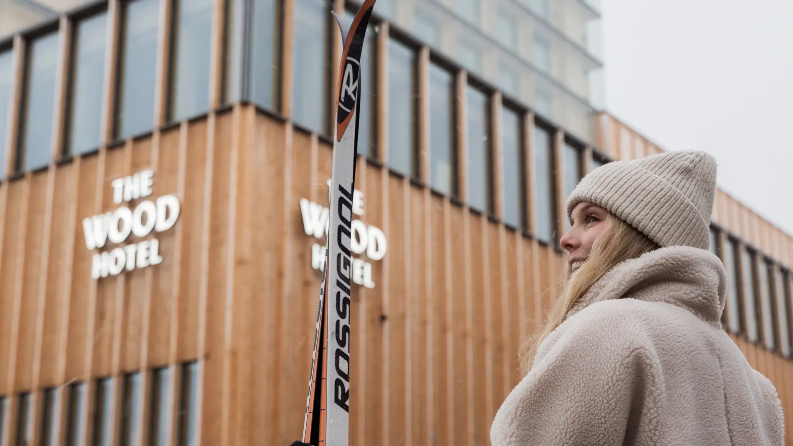 Skier hold on to a pair of cross-country skis standing in front of The Wood Hotel by Elite