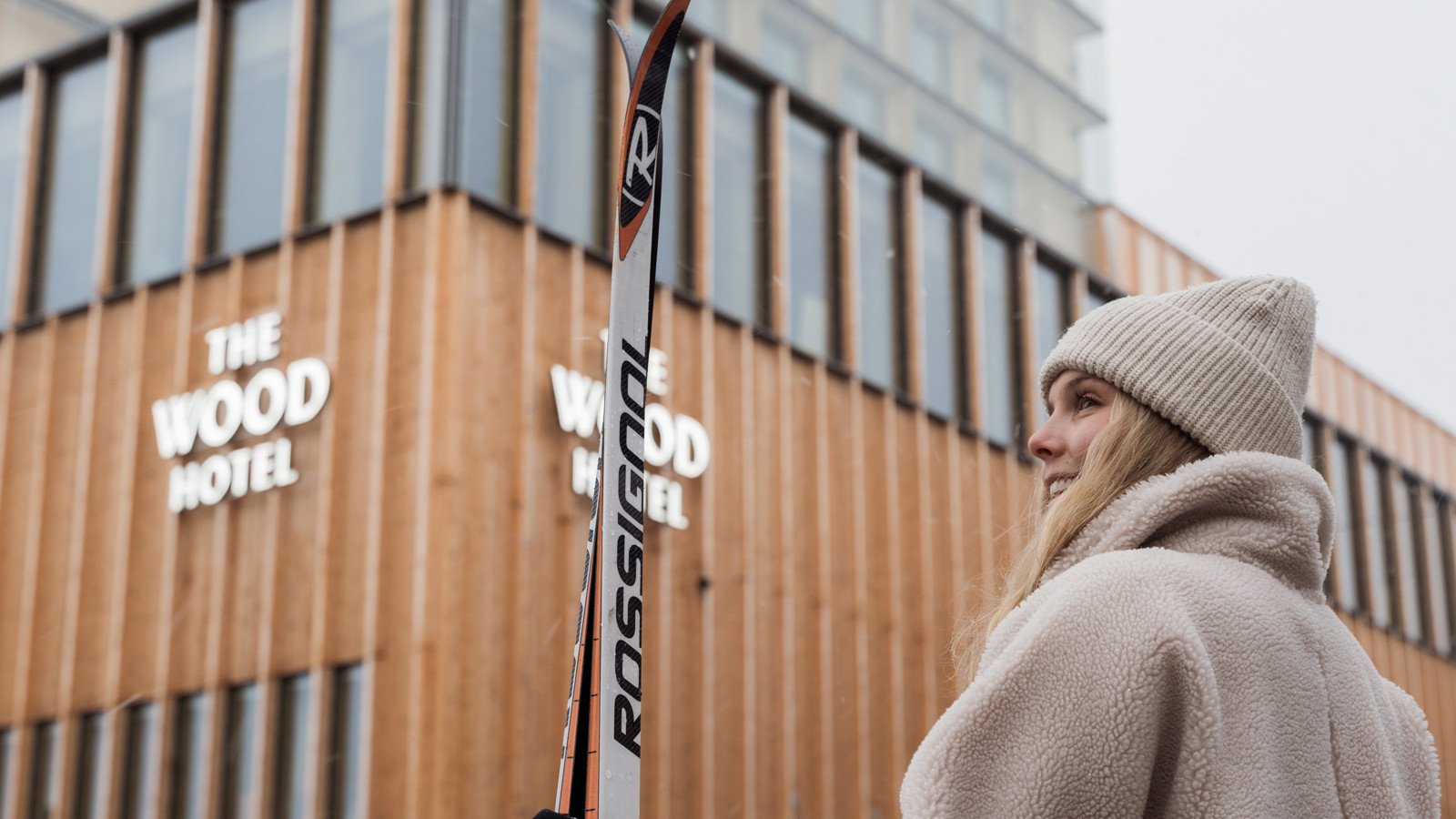 Skier hold on to a pair of cross-country skis standing in front of The Wood Hotel by Elite
