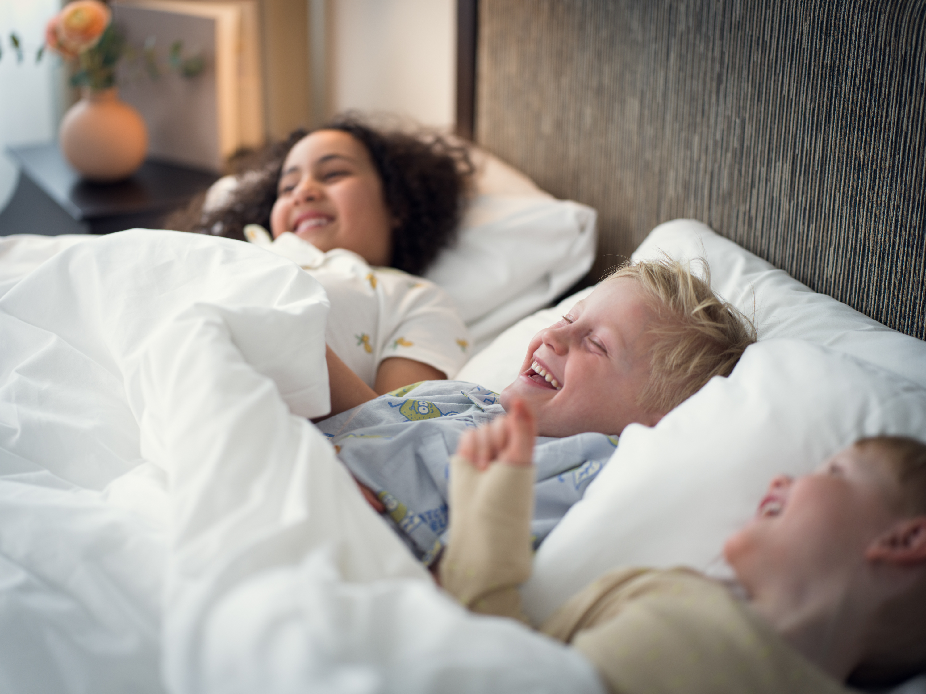 Three children lying down and laughing in a hotel bed