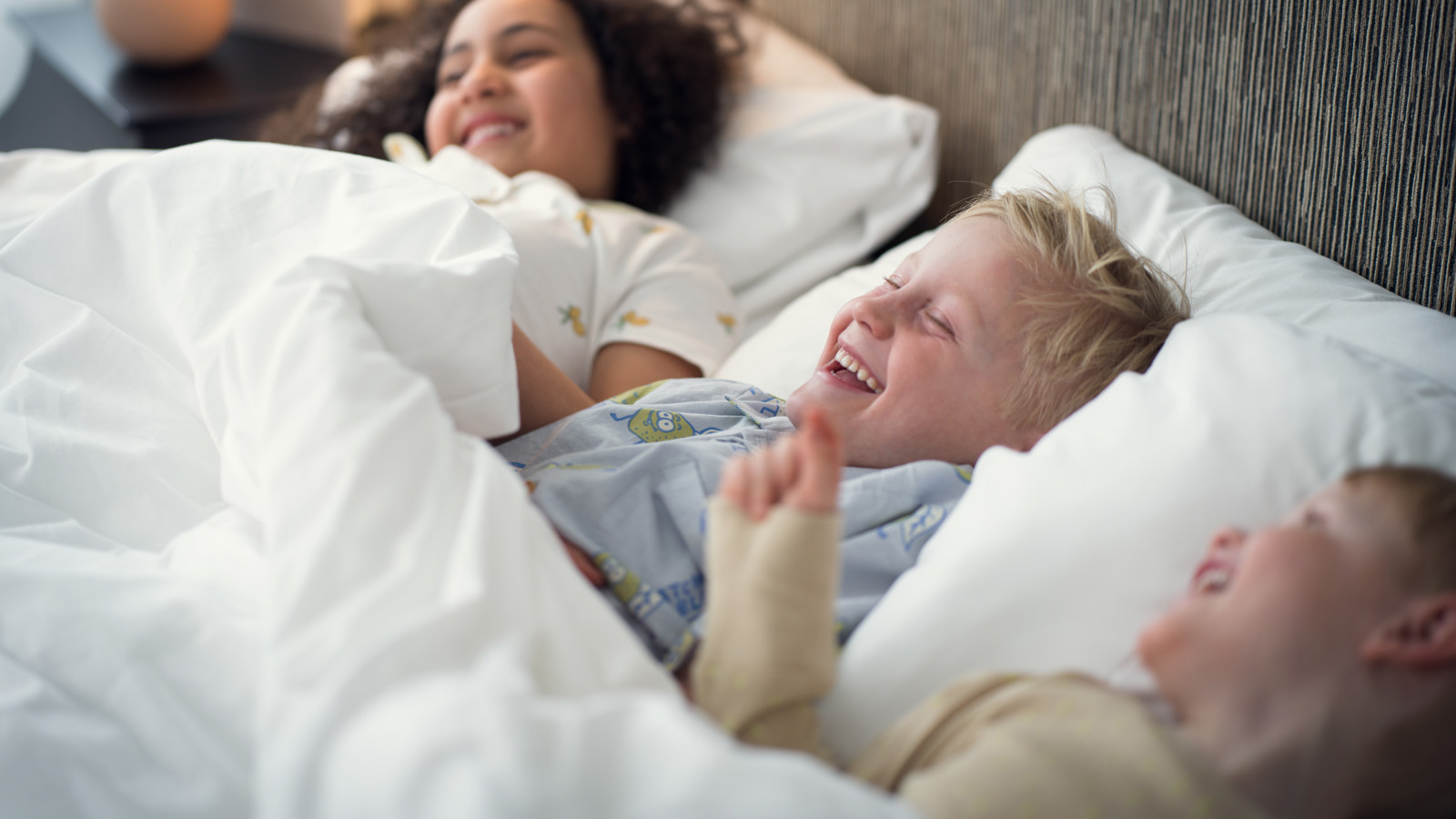 Three children lying down and laughing in a hotel bed