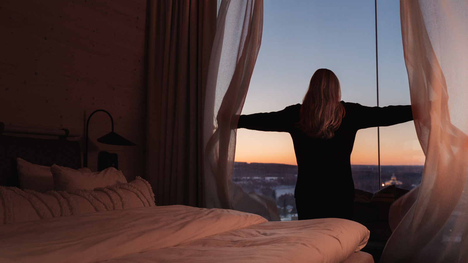 Woman opening curtains and seeing amazing view with sunrise