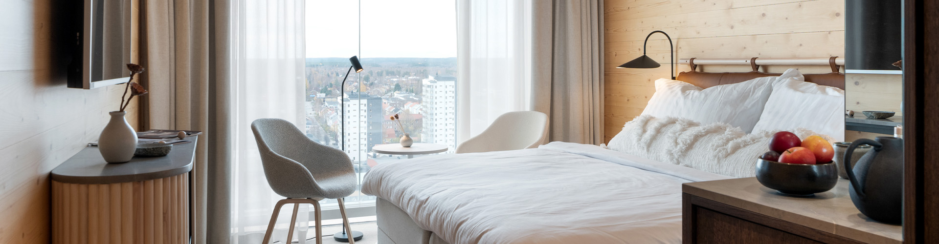 Cozy hotel room with double bed, TV, chairs and large windows overlooking Skellefteå