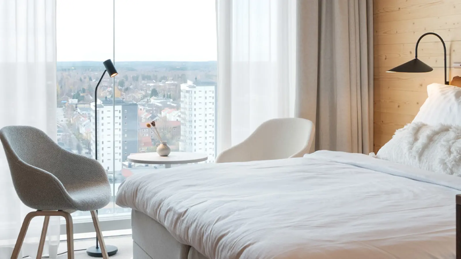Cozy hotel room with double bed, TV, chairs and large windows overlooking Skellefteå