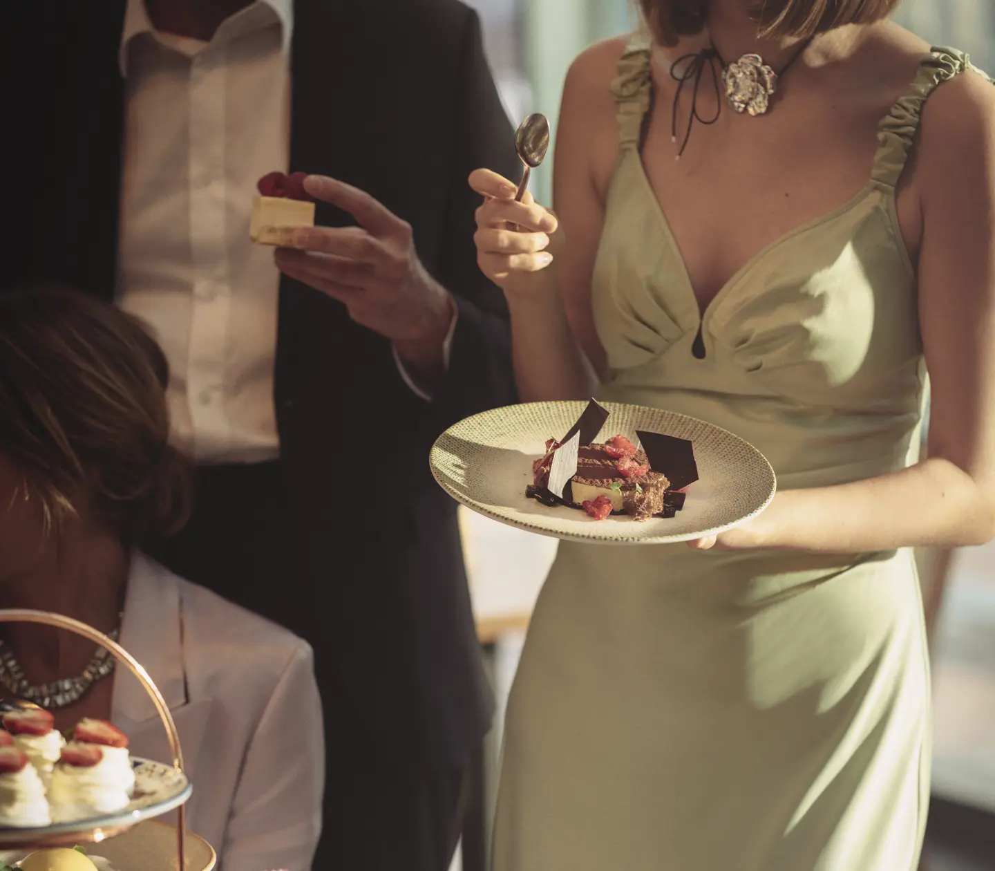 Personer i elegant klädsel deltar i en social tillställning och äter dessert.