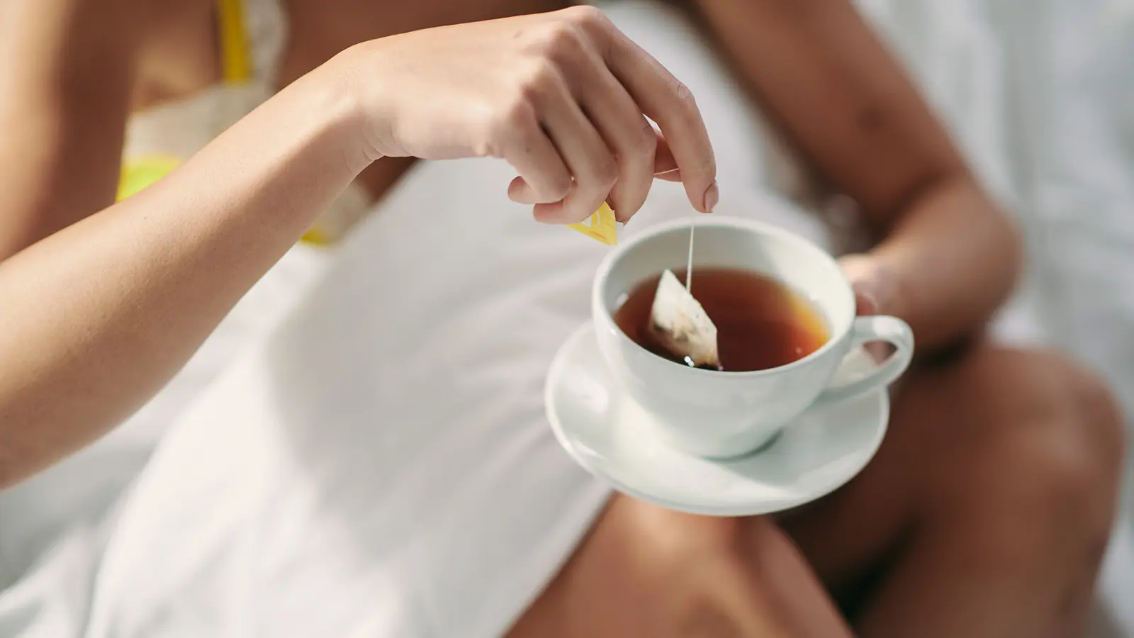 Kvinna som dricker en kopp te i sängen.