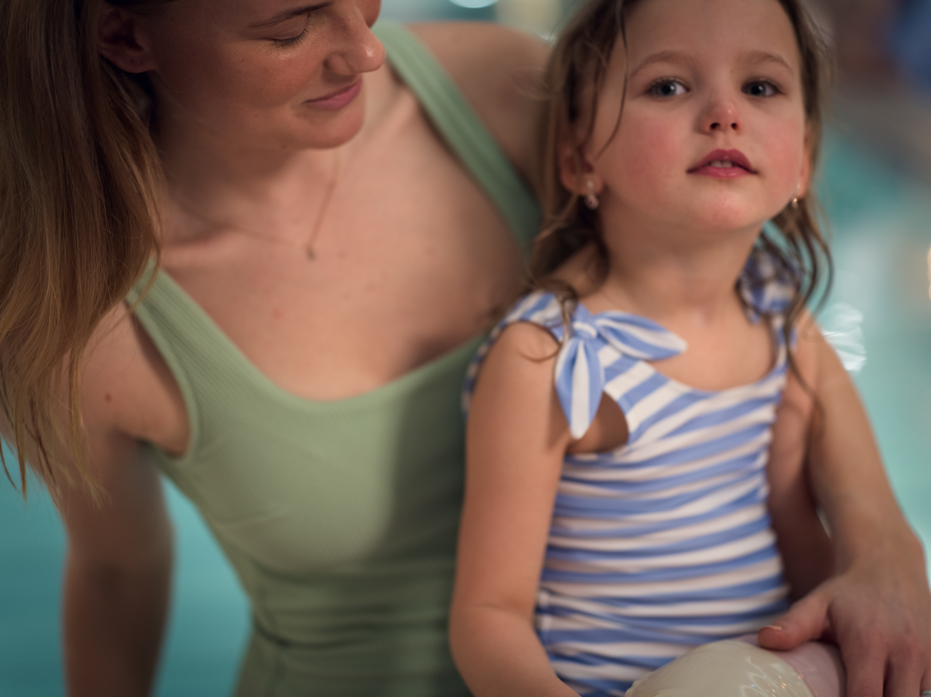 Flicka sitter på poolkanten tillsammans med en kvinna iklädda baddräkter.