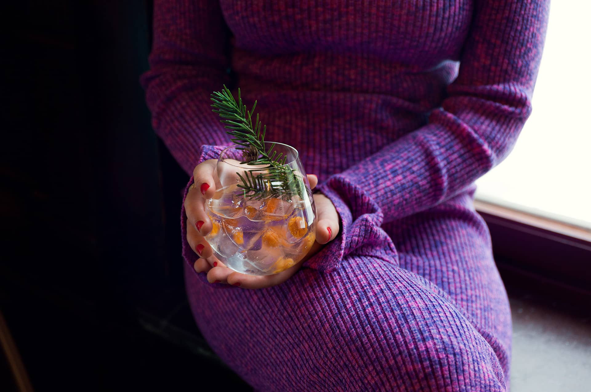 Bild på en drink med granskott hållandes av kvinna i lila klänning