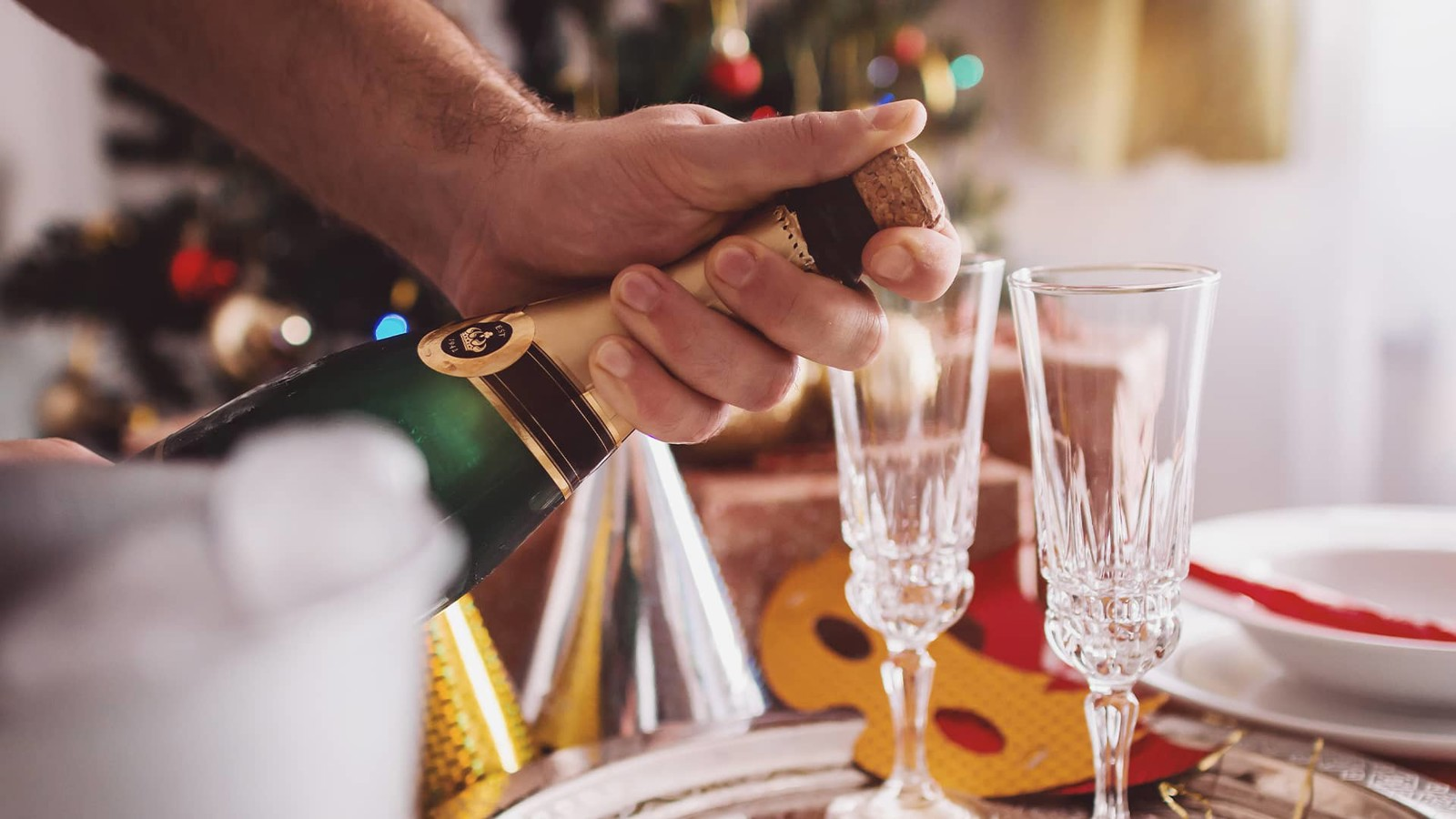Two champagne glasses and champagne bottle with New Year's accessories in the background