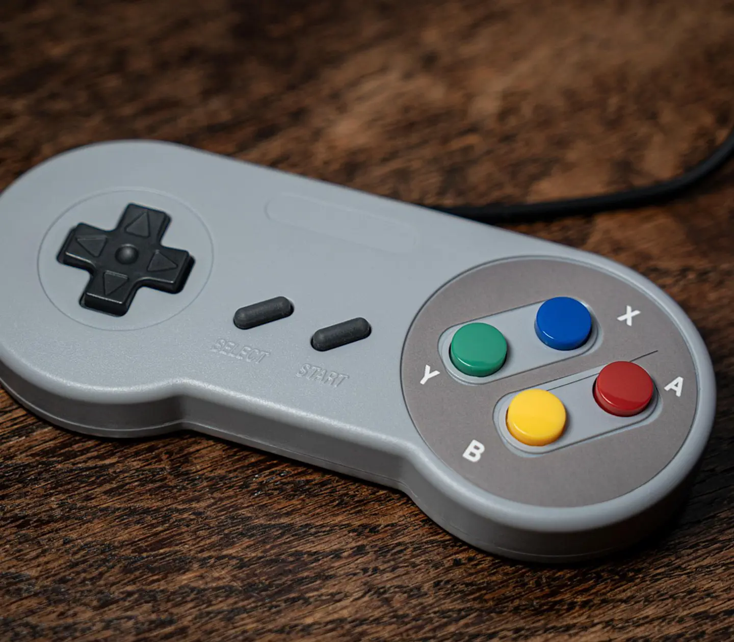 Grå retro spelkontroll med färgglada knappar på ett träbord