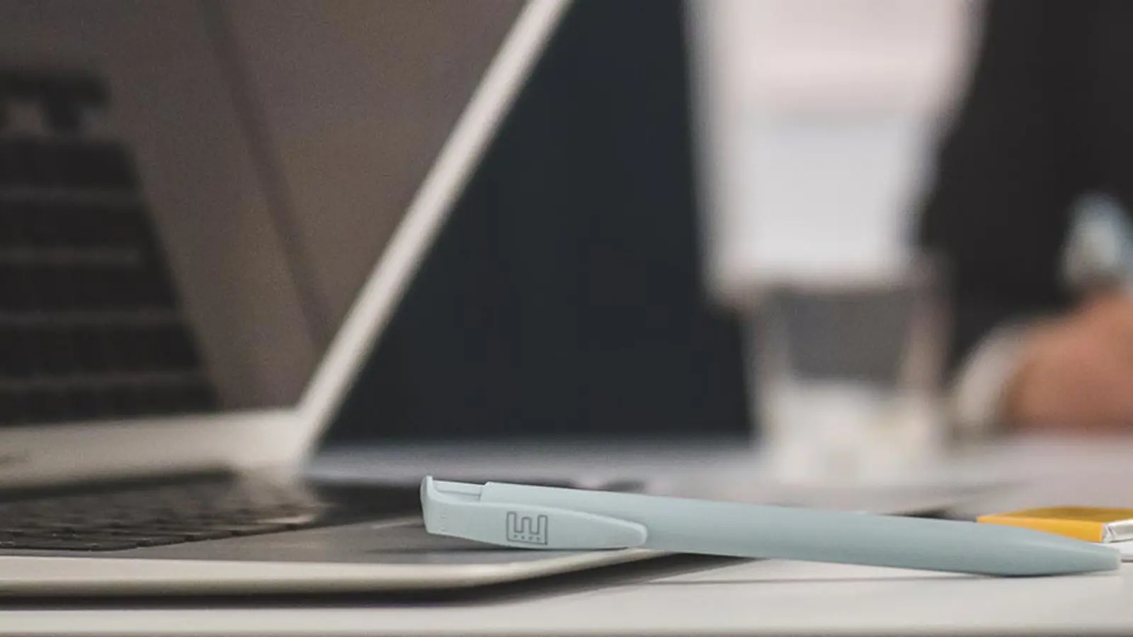 Laptop på ett konferensbord och en person som antecknar i bakgrunden