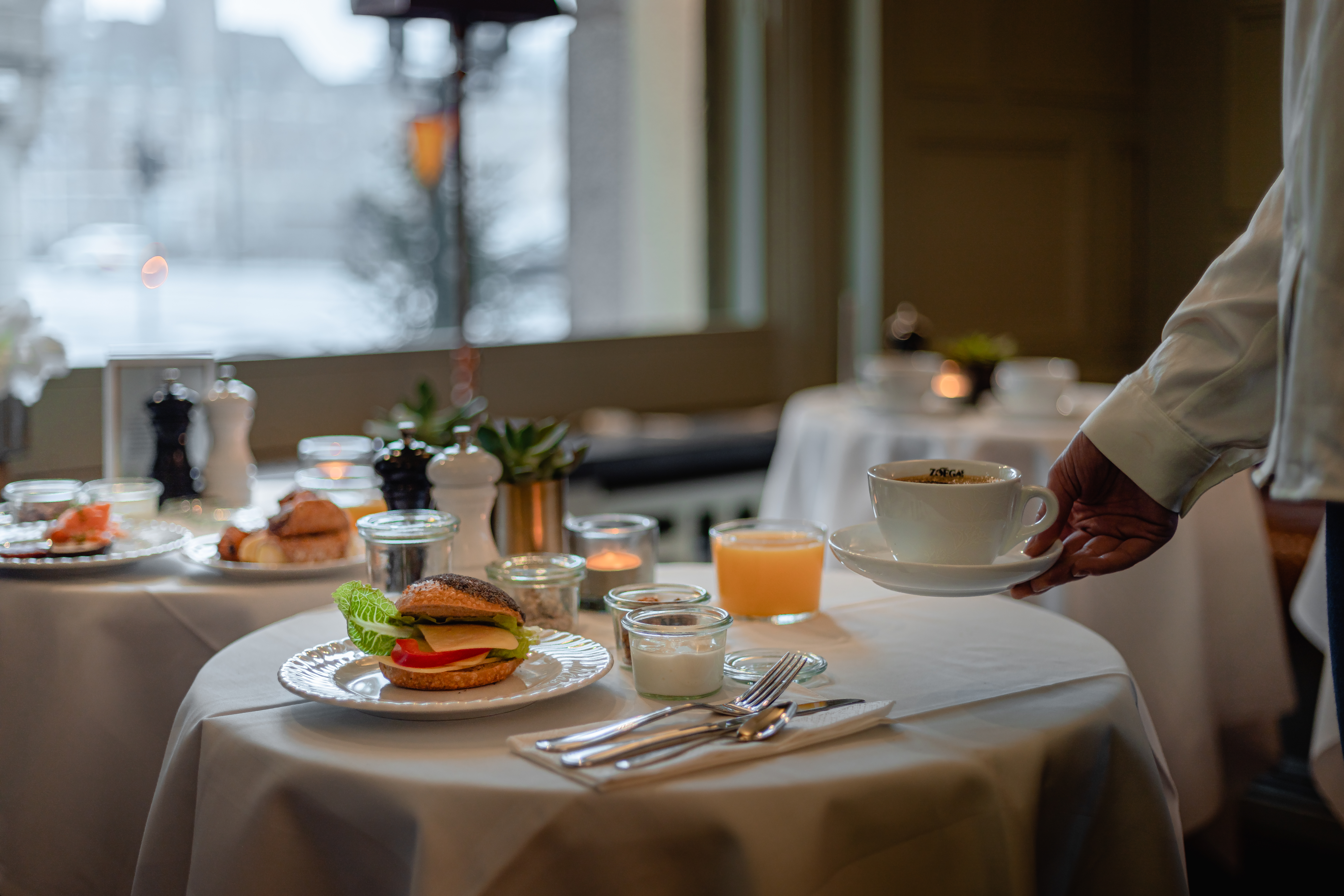 En servitör ställer ner en kaffe på ett bord med frukost uppdukat