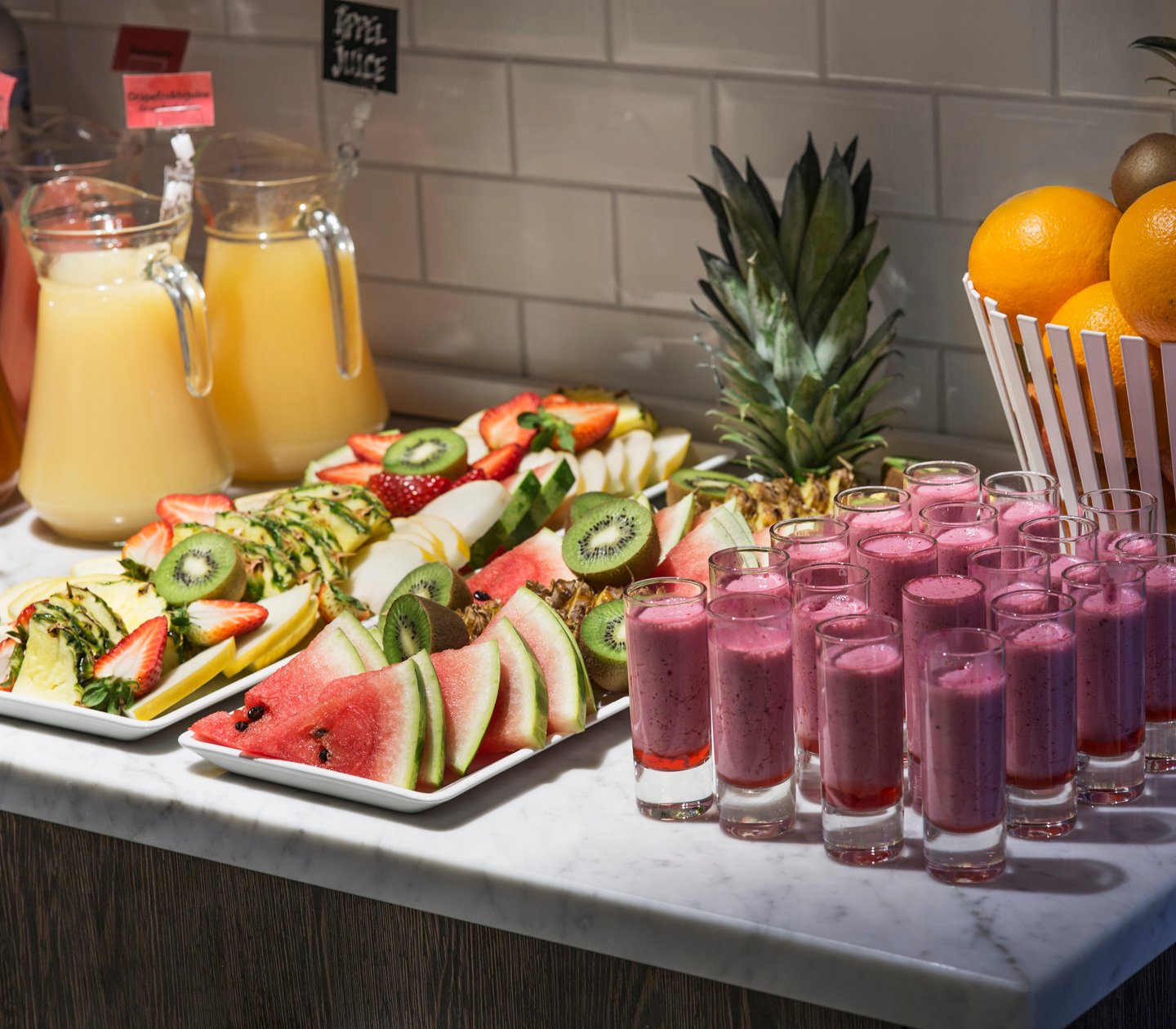 Fruits on a plate and several smoothie shots served on a breakfast buffet