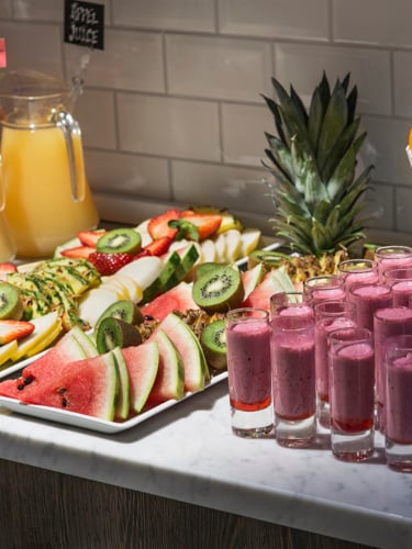 Fruits on a plate and several smoothie shots served on a breakfast buffet