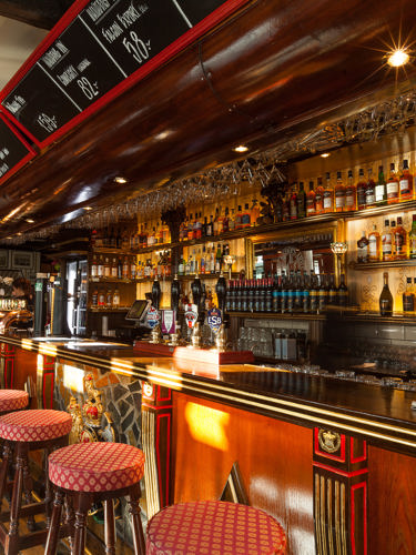 Klassisk engelsk pubmiljö med bar, mycket flaskor och barstolar