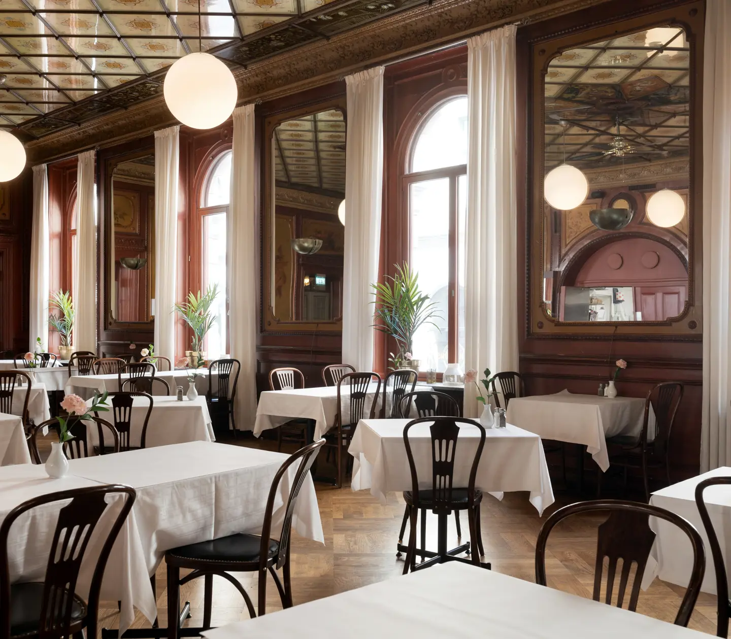 Nice dining room with mirrors on the walls and ceiling with large windows, many tables and chairs with white tablecloths