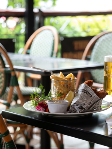 Kyckling och pommes med en öl serverad i en restaurang med rottingstolar