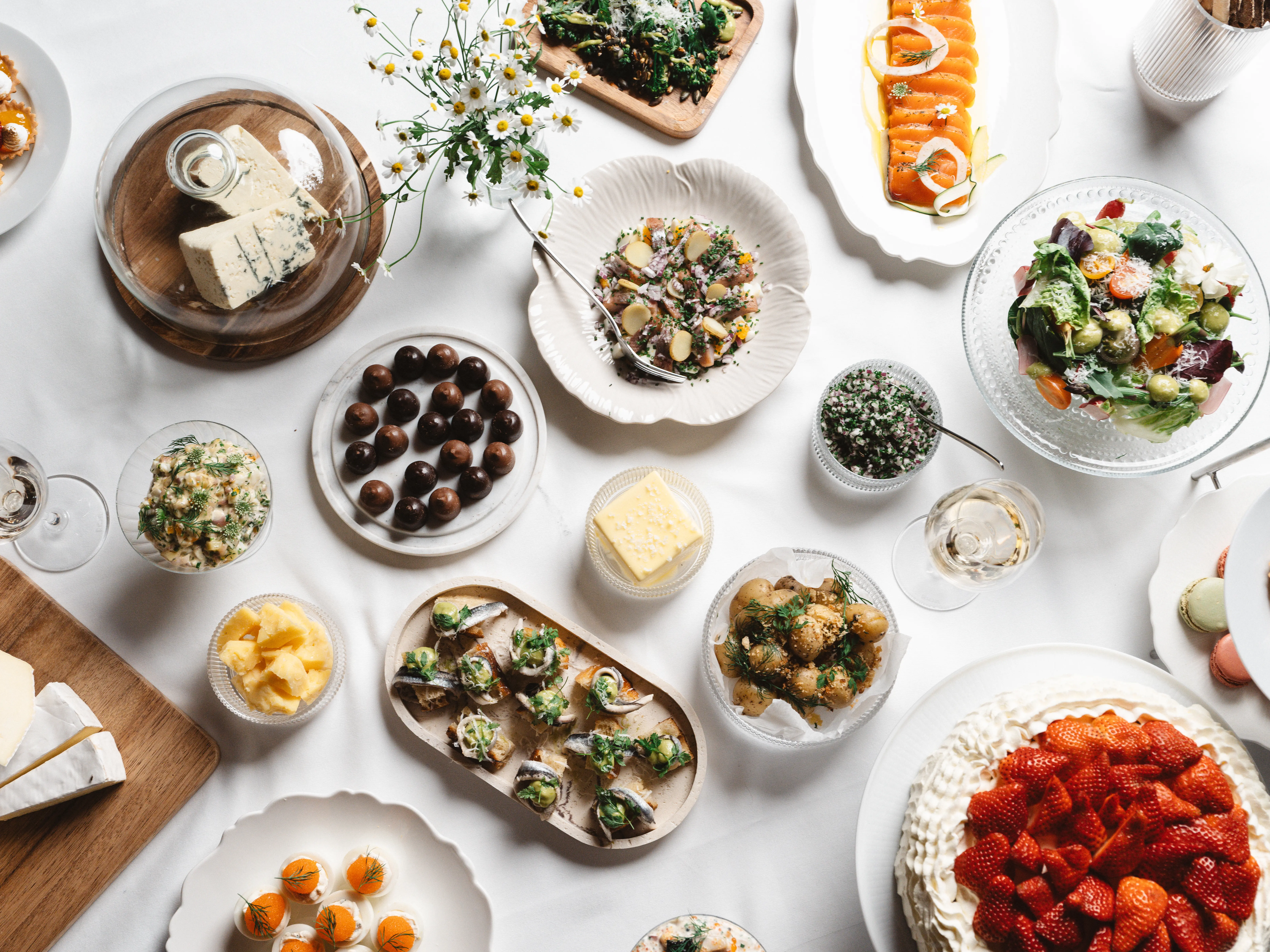 Swedish buffet with various dishes, including a cheese plate, salad, chocolate pralines, pickled herring, roasted potatoes, and strawberry cake on a set table