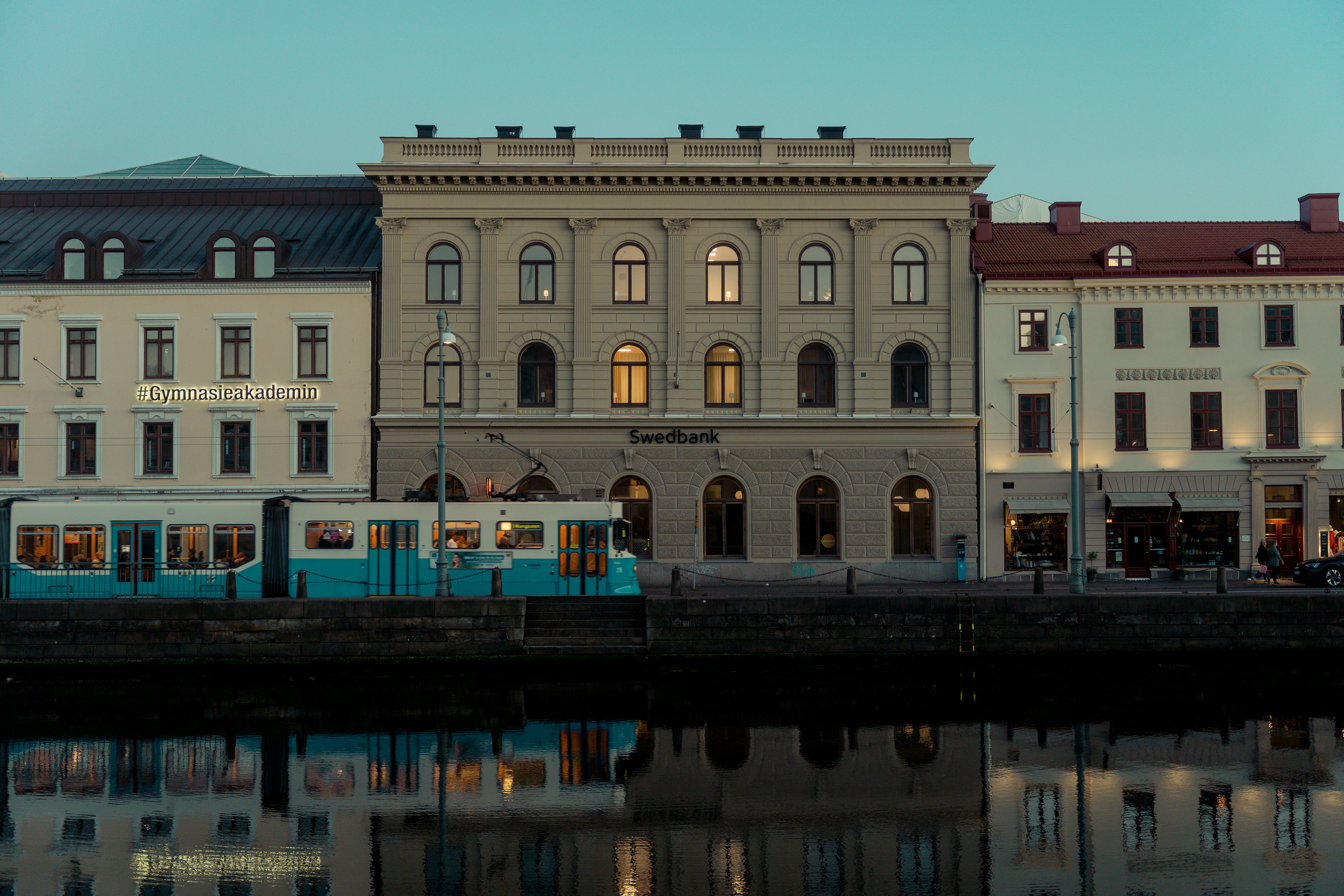 Blue tram on city street at sunset with building backdrop