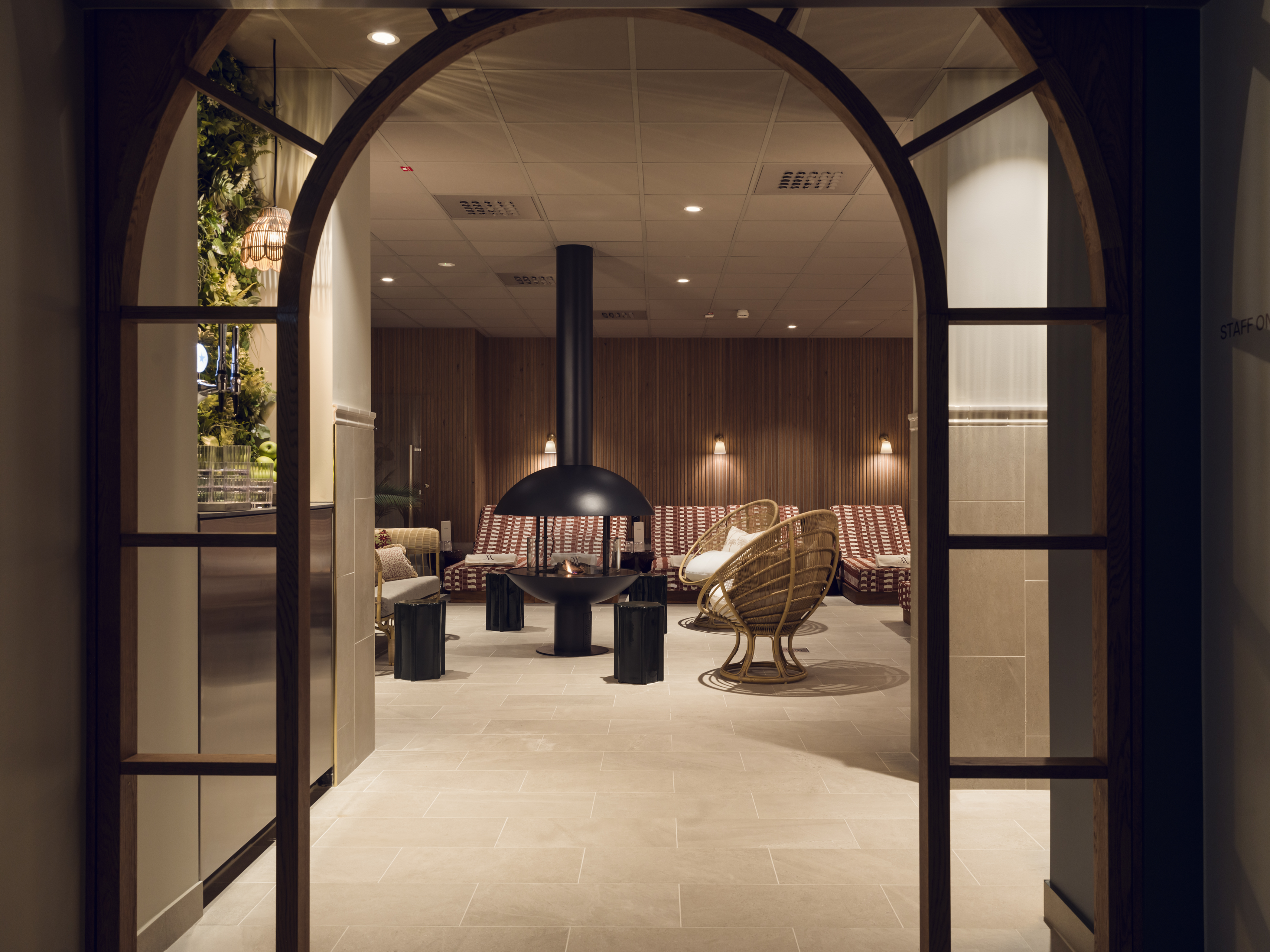 Modernt vardagsrum med öppen spis, rottingstolar och bekväma soffor, inramat av en valvformad dörröppning.