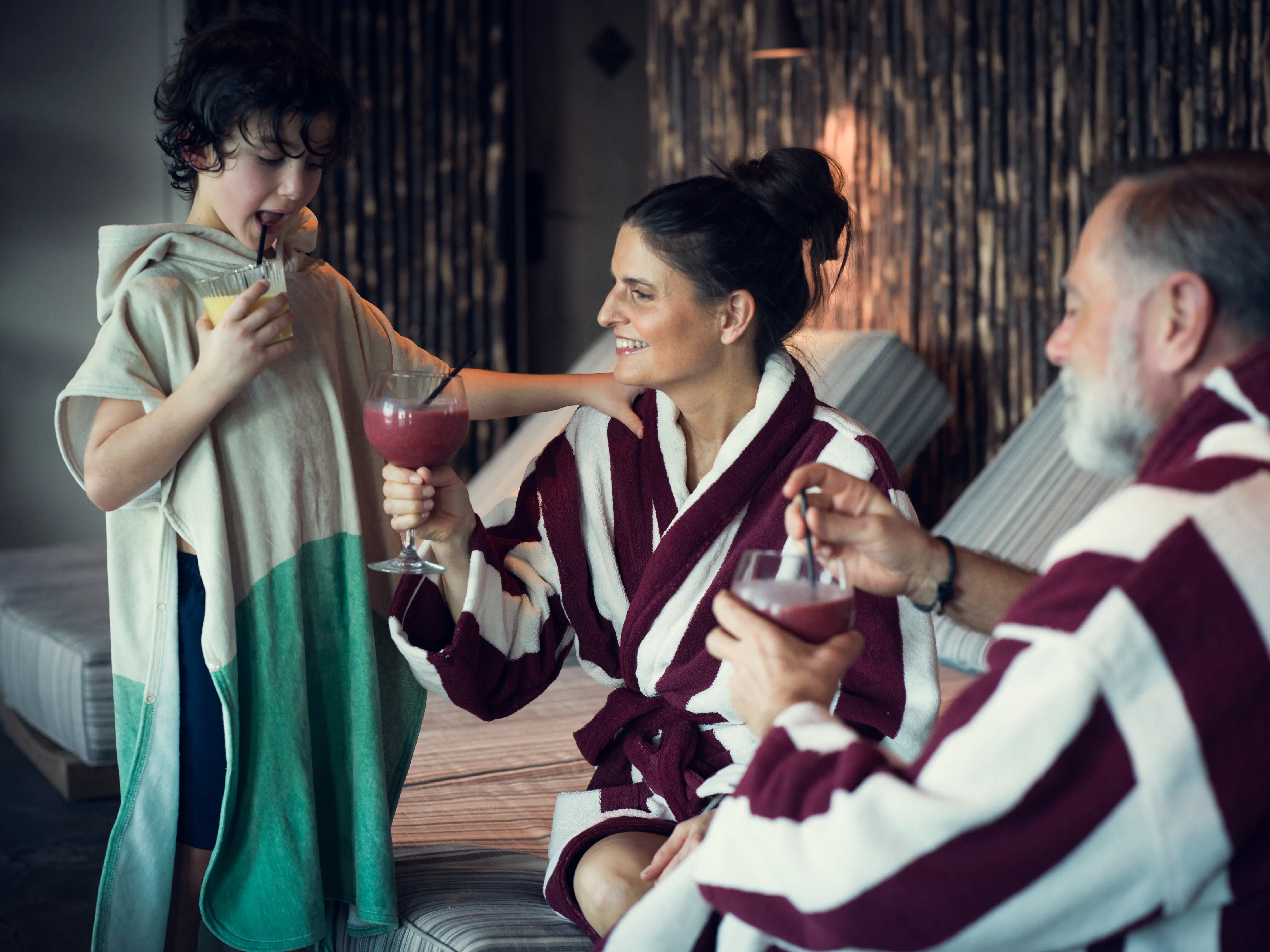 Två vuxna i badrockar och pojke i poncho på spa