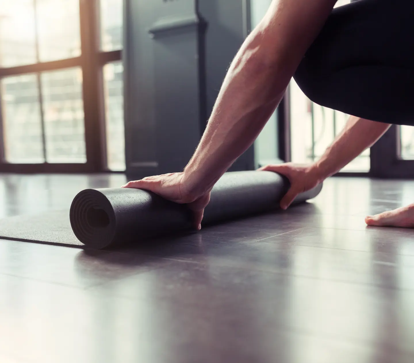 Person rullar ihop en blå yogamatta på trägolv.