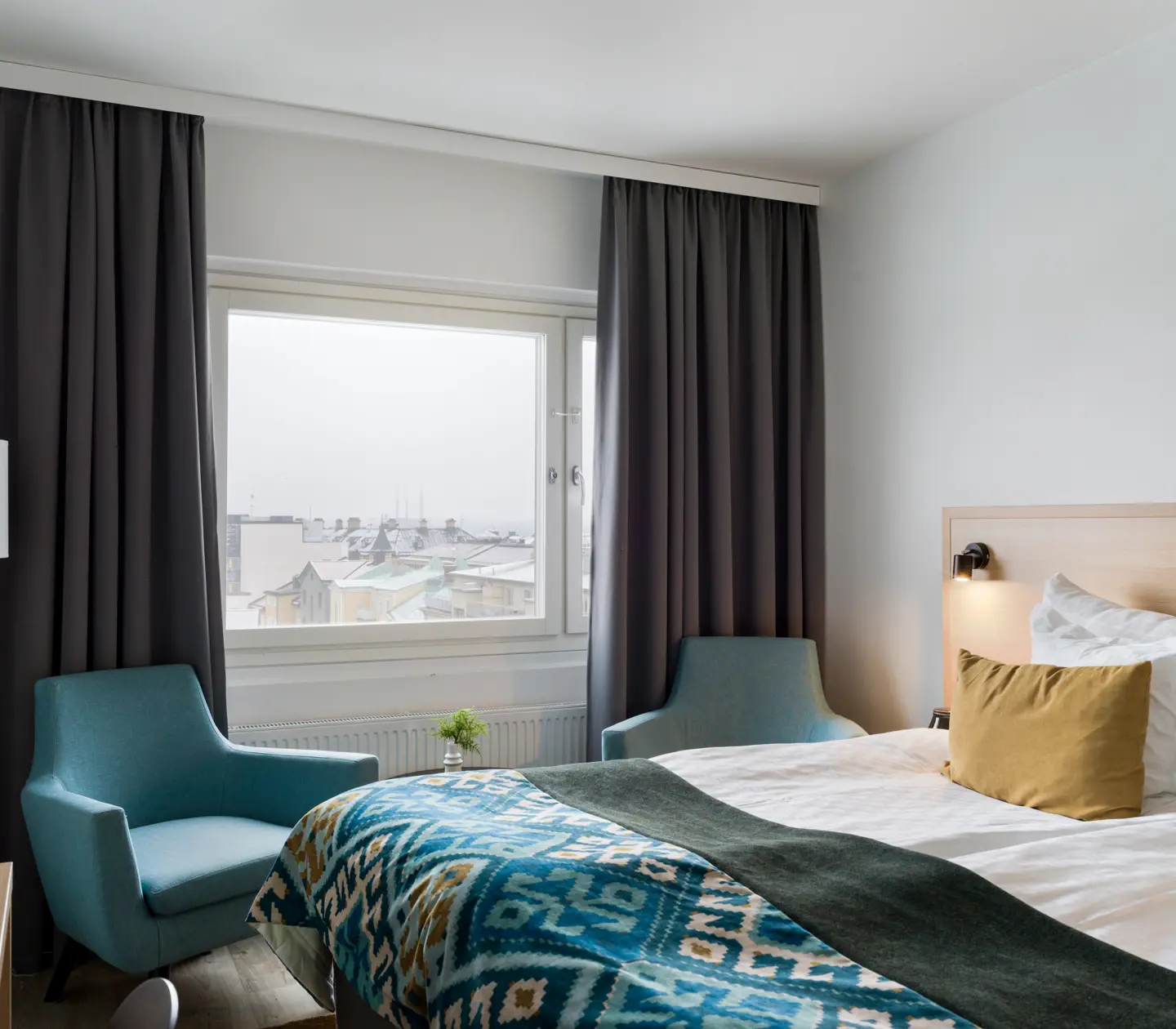 Ljust hotellrum med dubbelsäng, fåtöljer och fönster