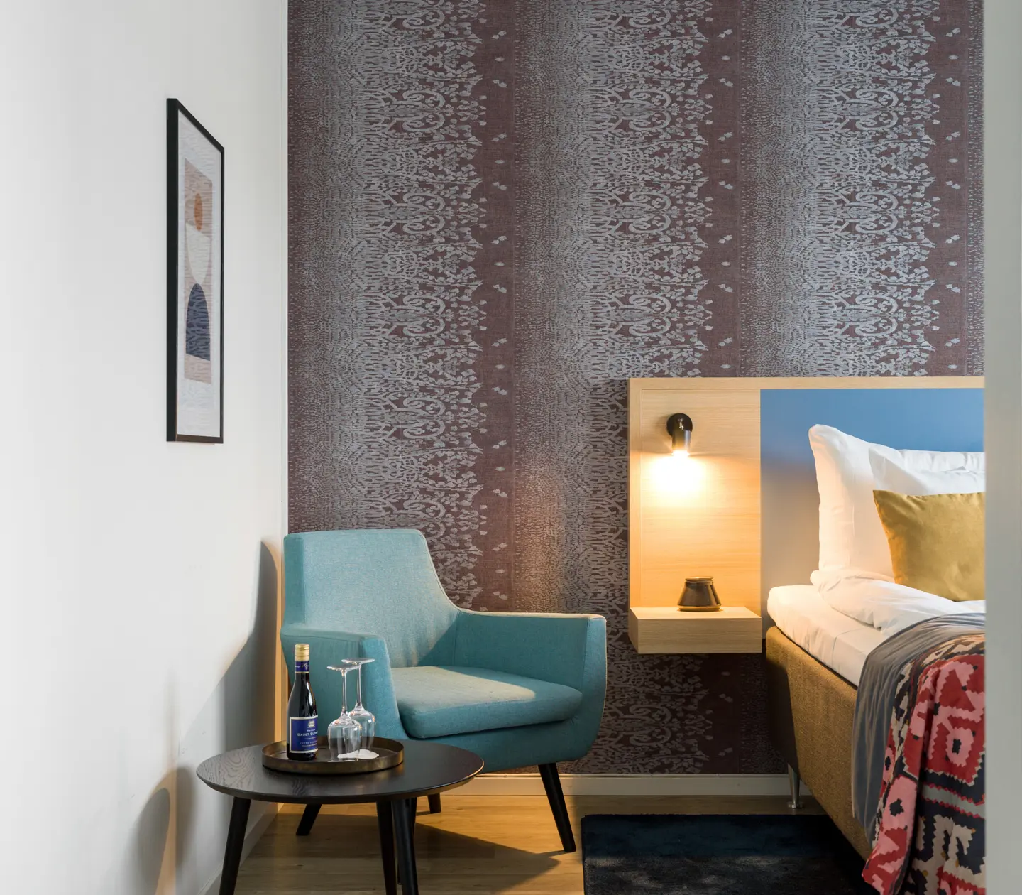 Hotellrum med fondvägg, del av säng och fåtölj