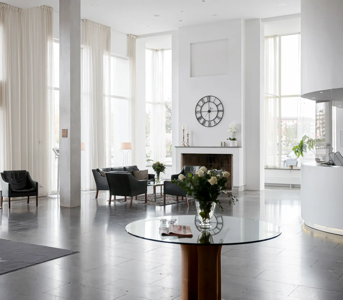 Ljus hotellobby med receptionsdisk, brasa och höga fönster