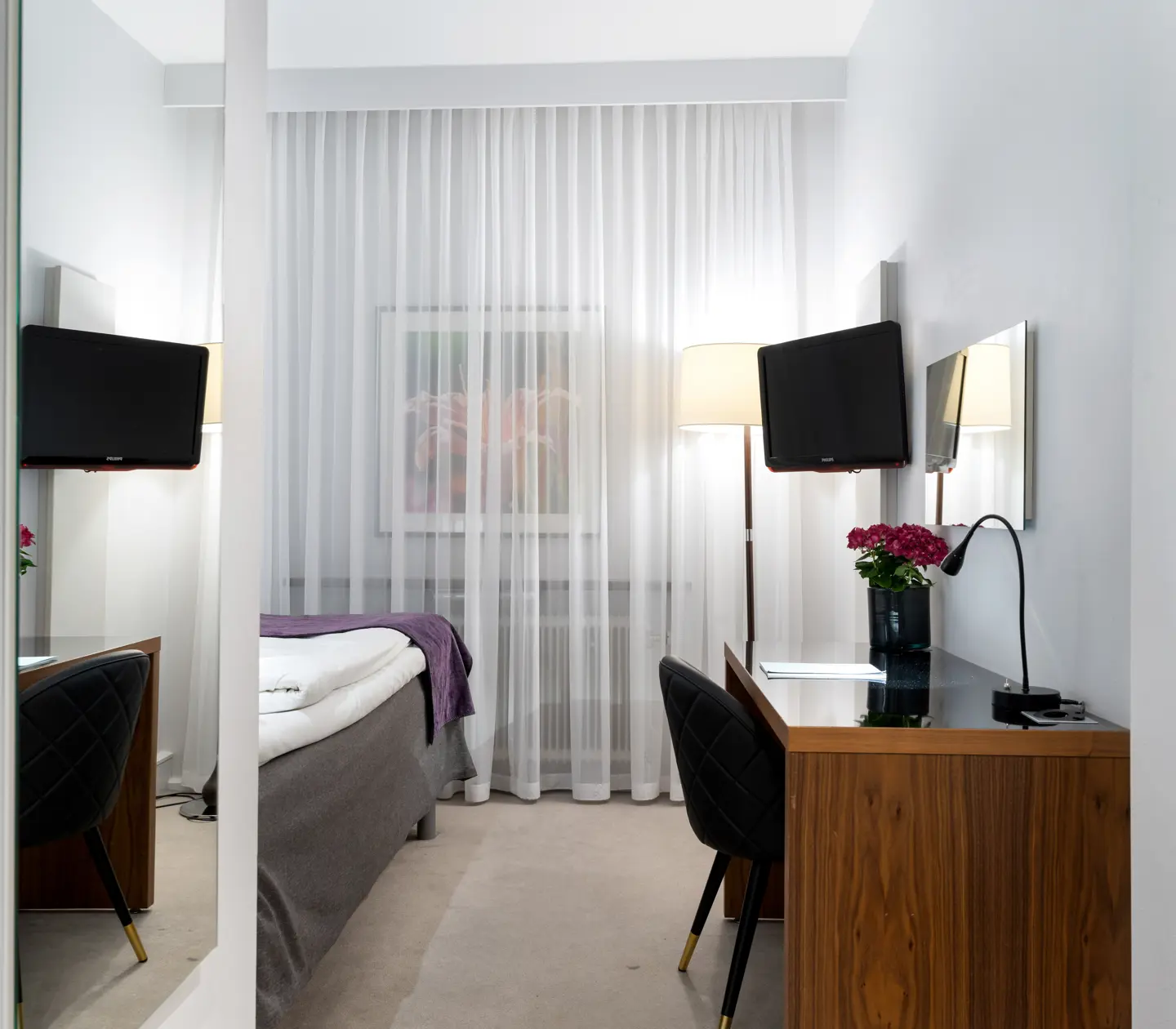 Hotellrum med enkelsäng, skrivbord och tv