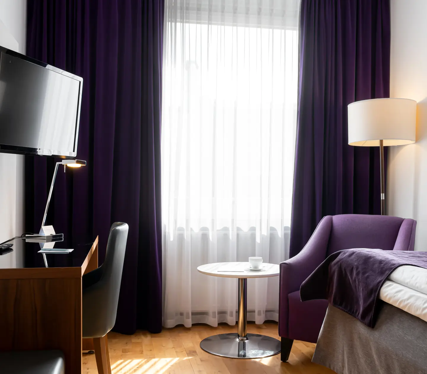 Hotellrum med enkelsäng, skrivbord och fåtölj