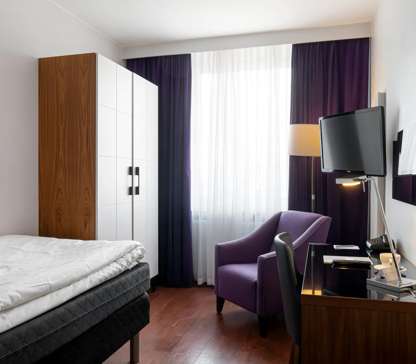 Hotellrum med enkelsäng, skrivbord och garderob
