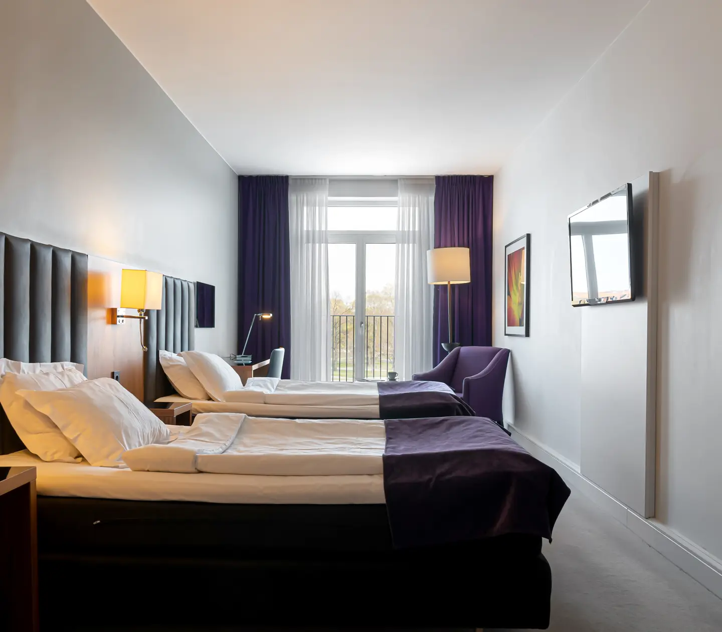 Hotellrum med två enkelsängar, fåtöljer och tv
