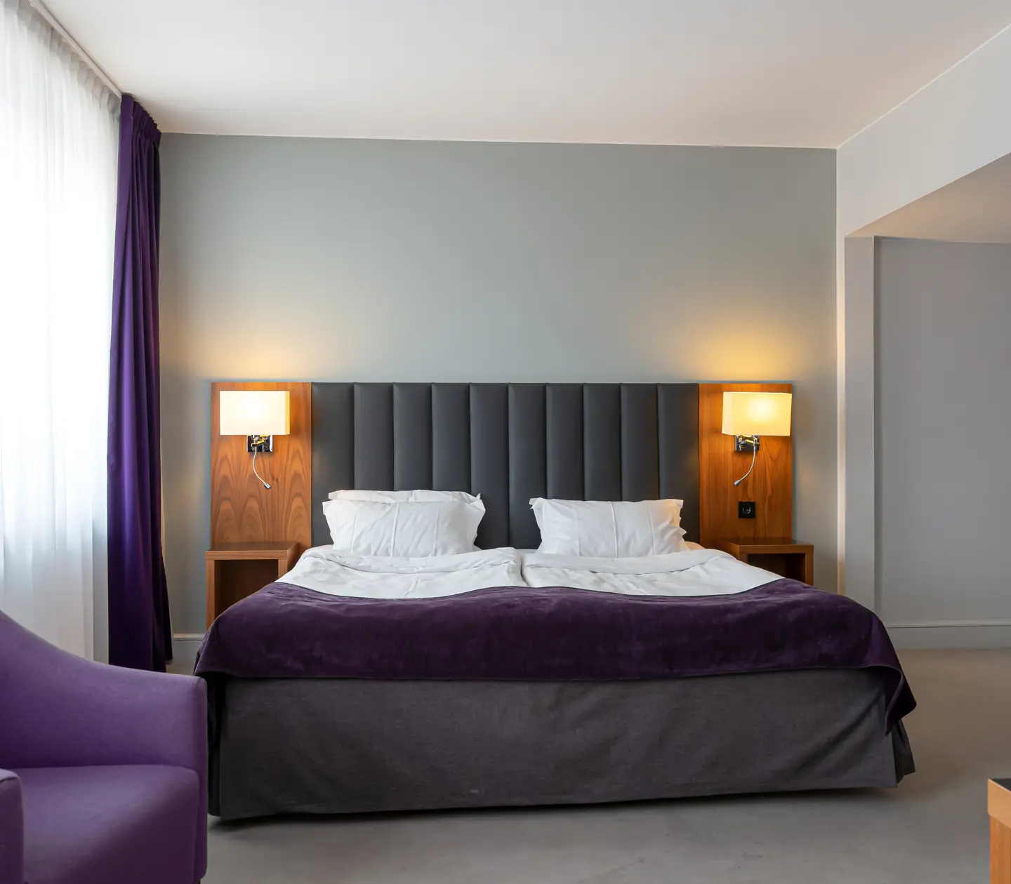 Hotellrum med dubbelsäng, fåtölj och sänglampor