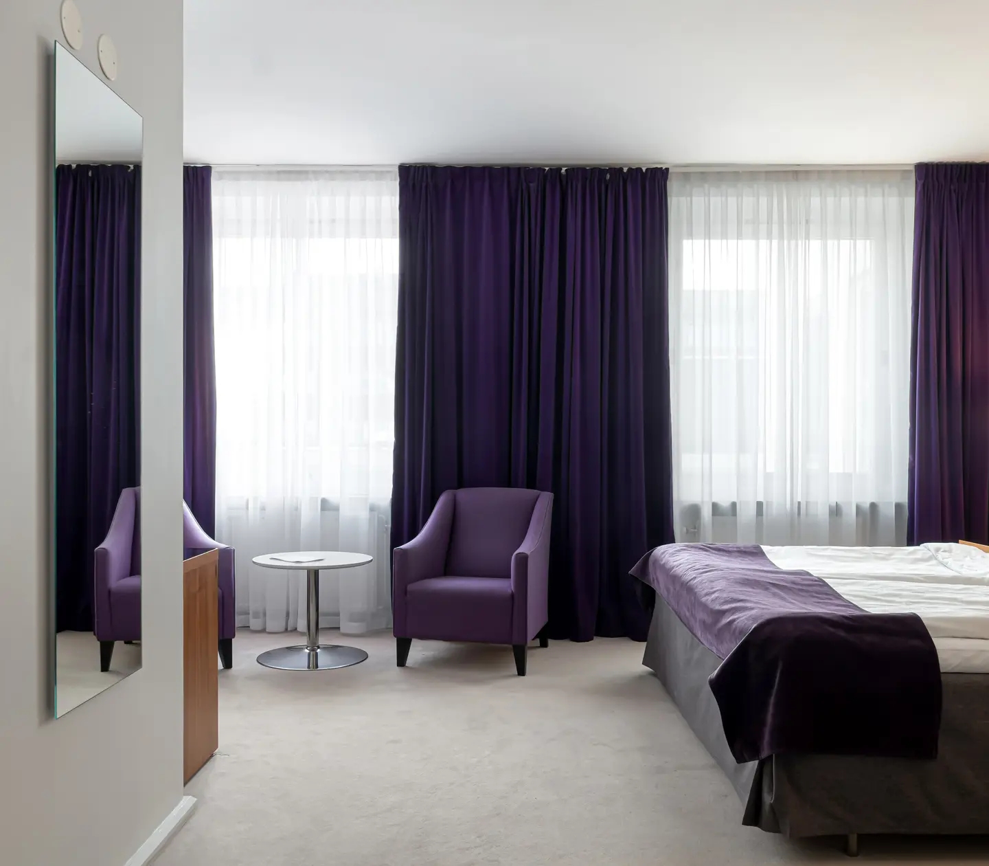 Hotellrum med dubbelsäng, fåtöljer och spegel