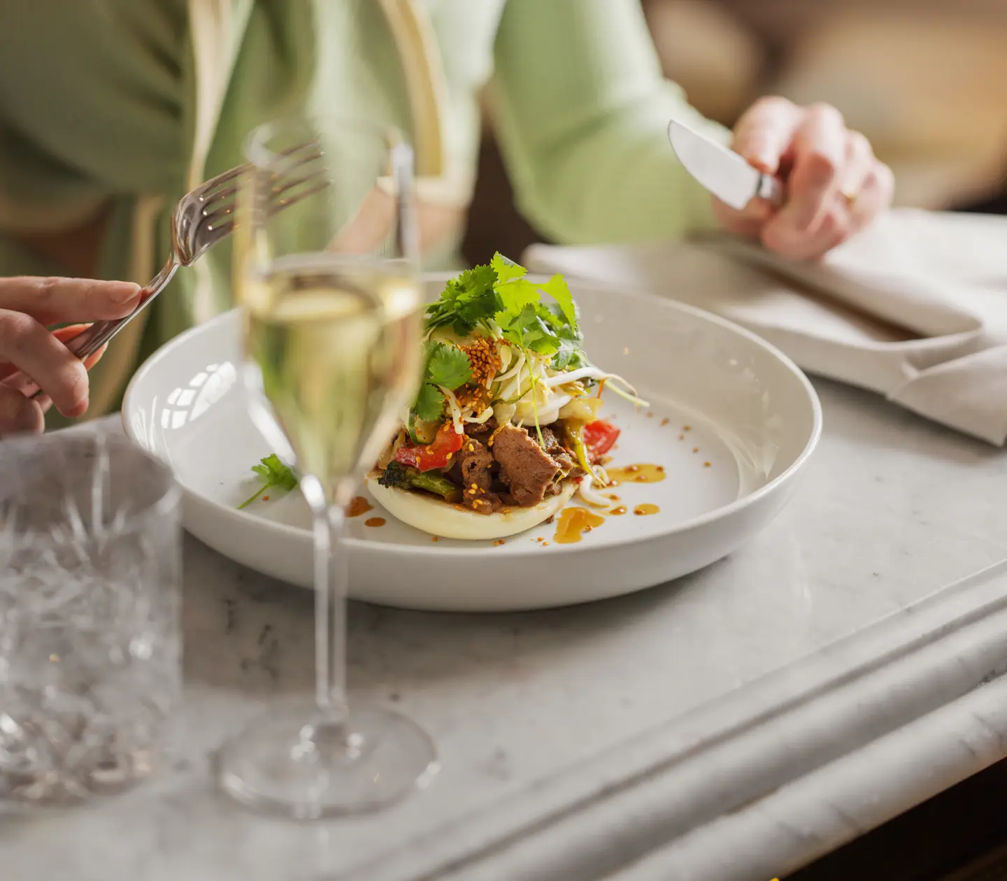 Kvinna som har en tallrik med mat och ett champagneglas framför sig
