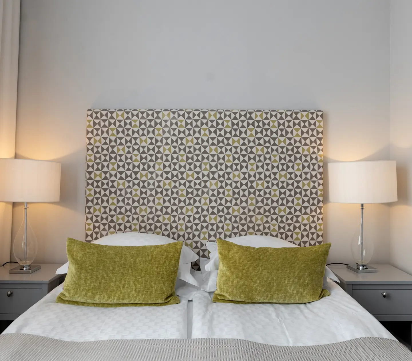 Hotellrum med dubbelsäng, gröna kuddar och sänglampor