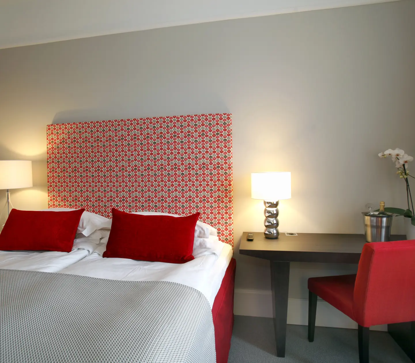 Hotellrum med röda detaljer, säng och skrivbord