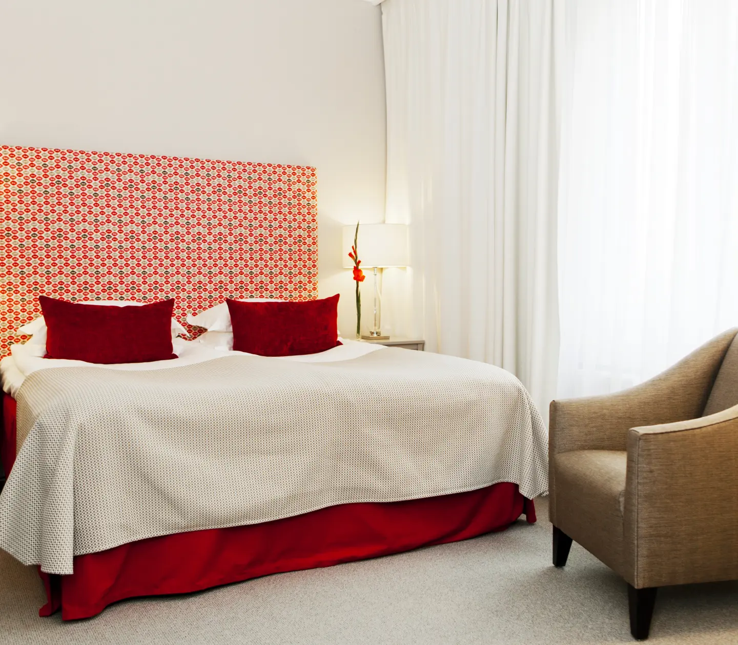 Hotellrum med säng, röd sänggavel och fåtölj
