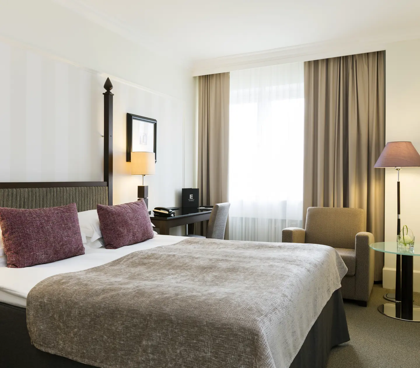 Mysigt hotellrum med dubbelsäng, skrivbord och fåtölj
