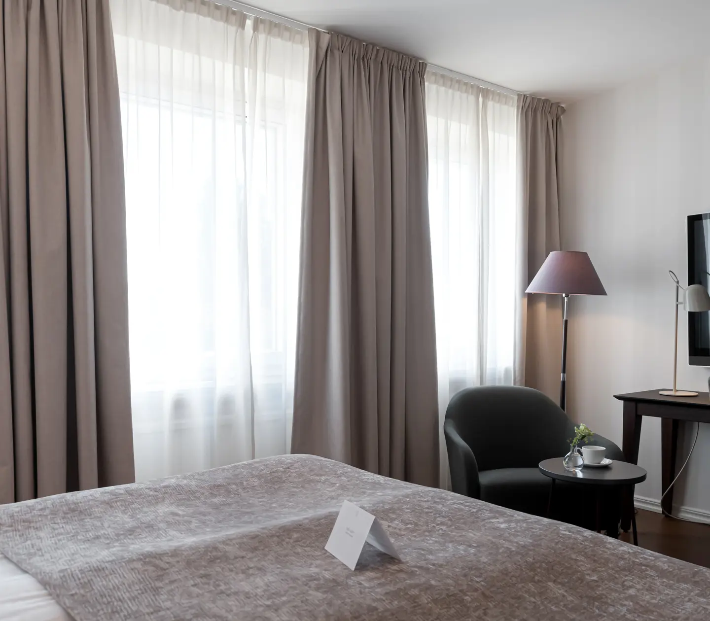 Hotellrum med skrivbord, fåtölj och stora fönster