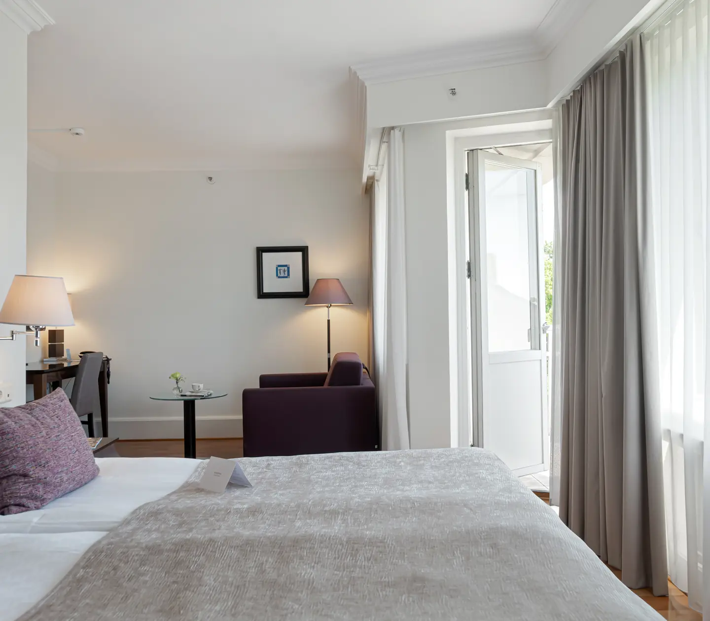 Mysigt hotellrum med dubbelsäng, fåtölj och balkongdörr