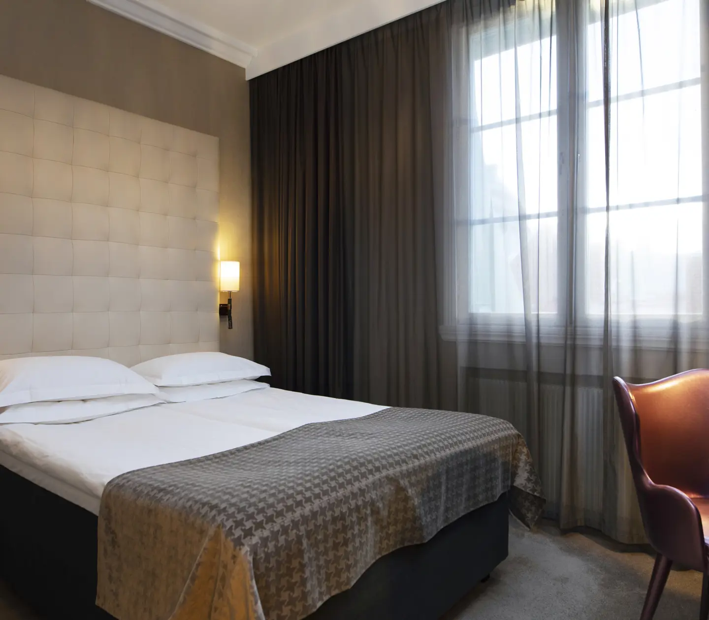 Hotellrum med säng, stor sänggavel och gardiner längs väggen