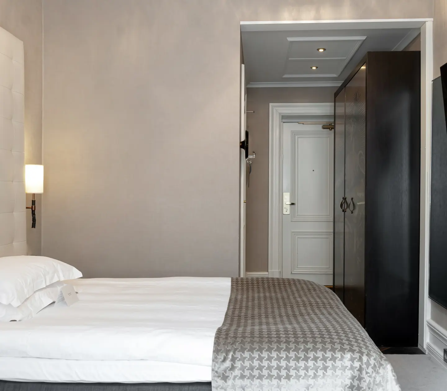Ljust hotellrum med säng, tv och garderob