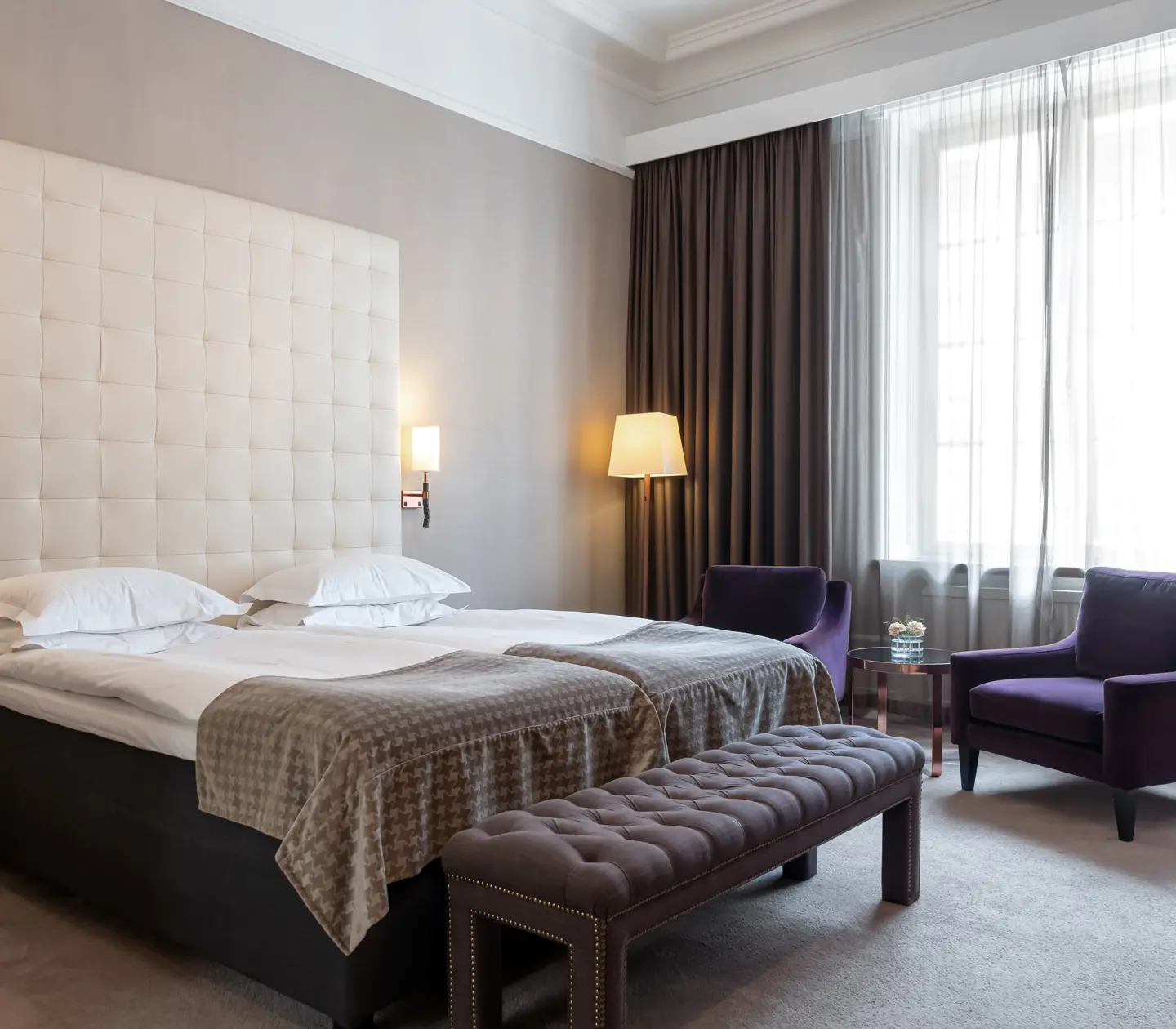 Hotellrum med säng, stor sänggavel och lila fåtöljer