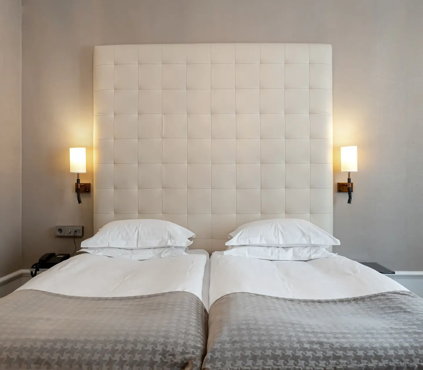 Ljust hotellrum med säng, stor sänggavel och sänglampor
