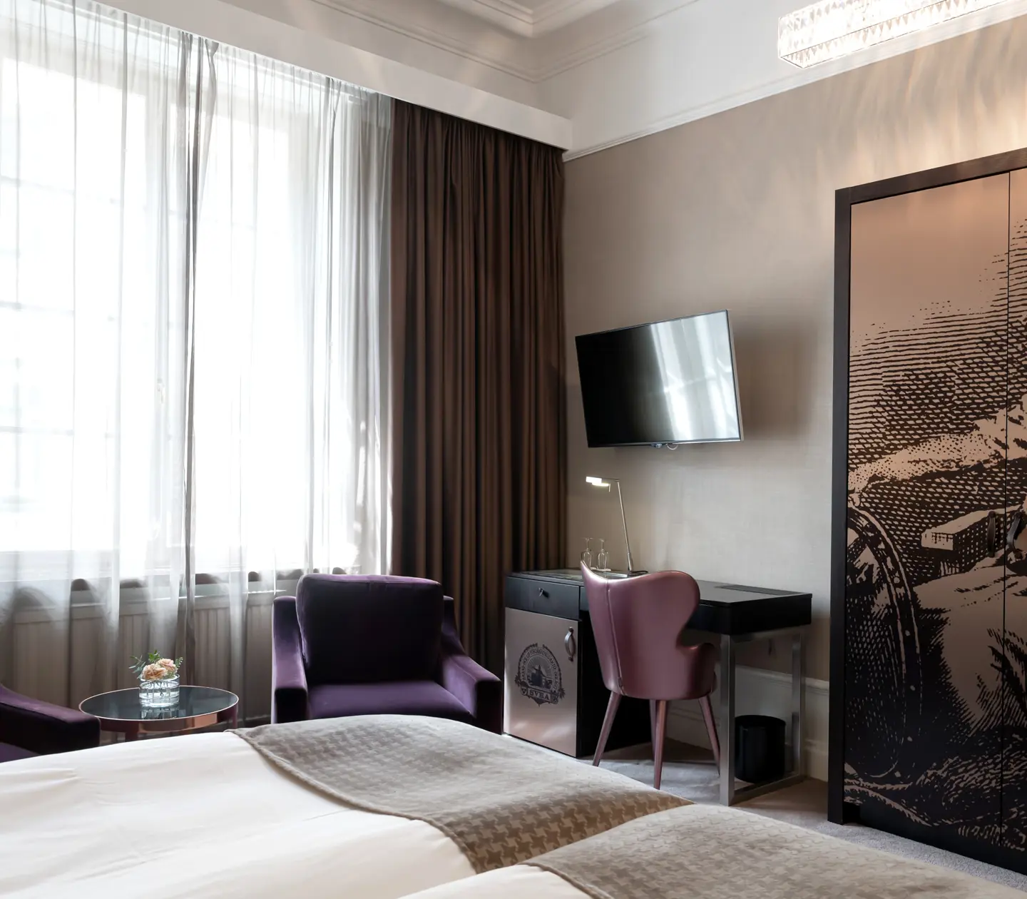 Ljust hotellrum med lila fåtöljer, skrivbord och garderob